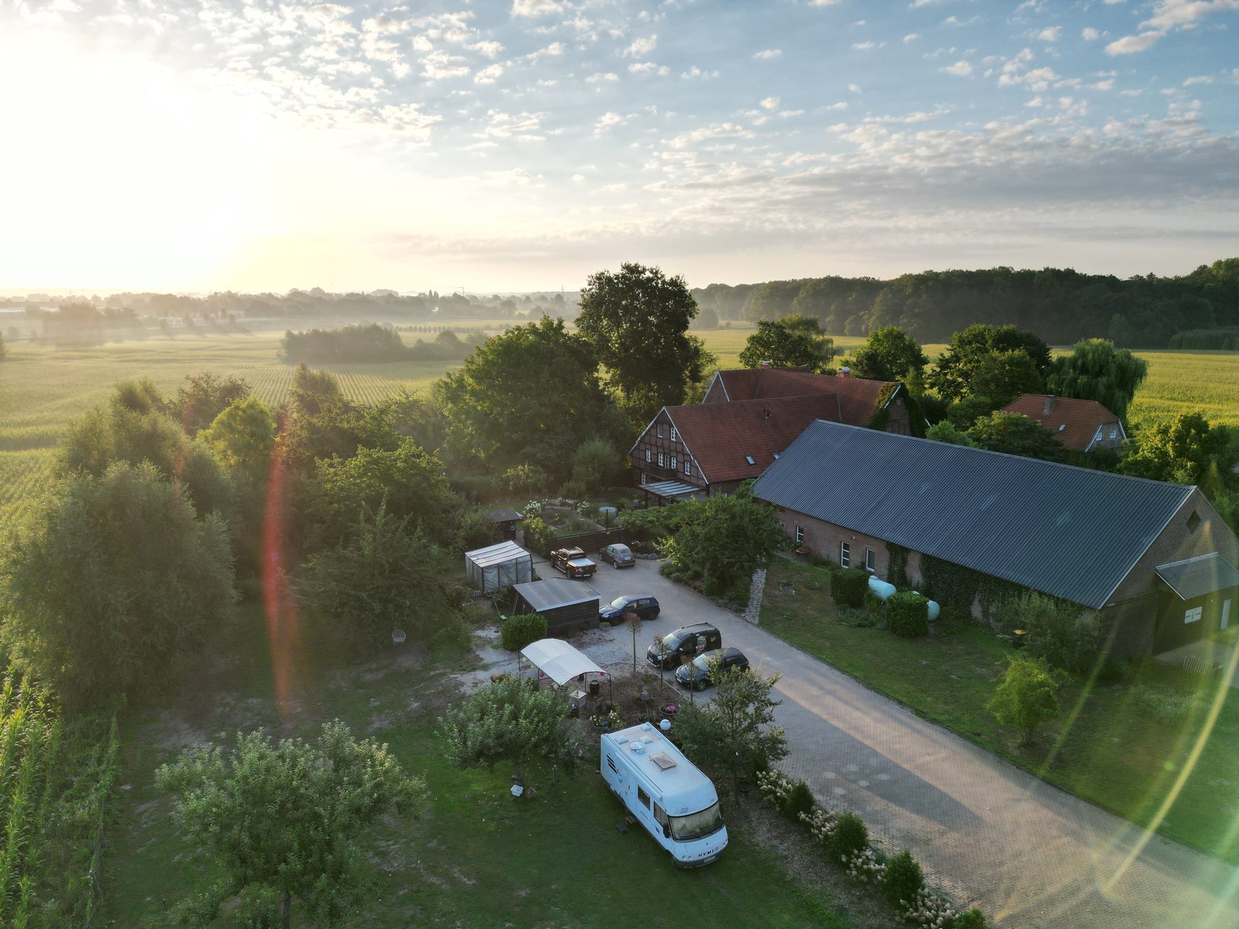 Luftaufnahme des Weberhofs am frühen Morgen: Fachwerkhof, Wohnmobil auf der Obstwiese, dahinter Felder und Nebel Richtung Münster.