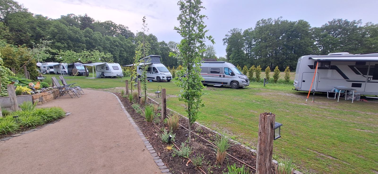 Reihe von Wohnmobilen und Campern auf der Wiese, davor ein Kiesweg mit Laternen.